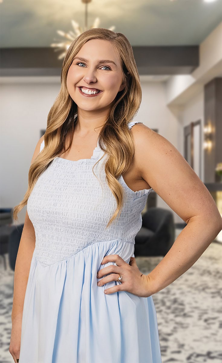 Smiling woman with long blonde hair in a white dress at Arya Medical Spa.