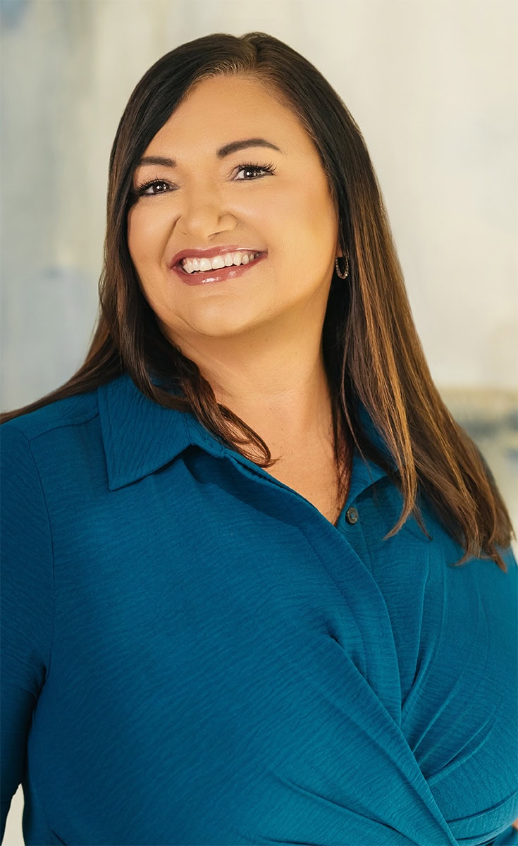 Portrait of Maura, a woman with dark hair and a bright smile, in a professional setting at Arya Medical Spa.