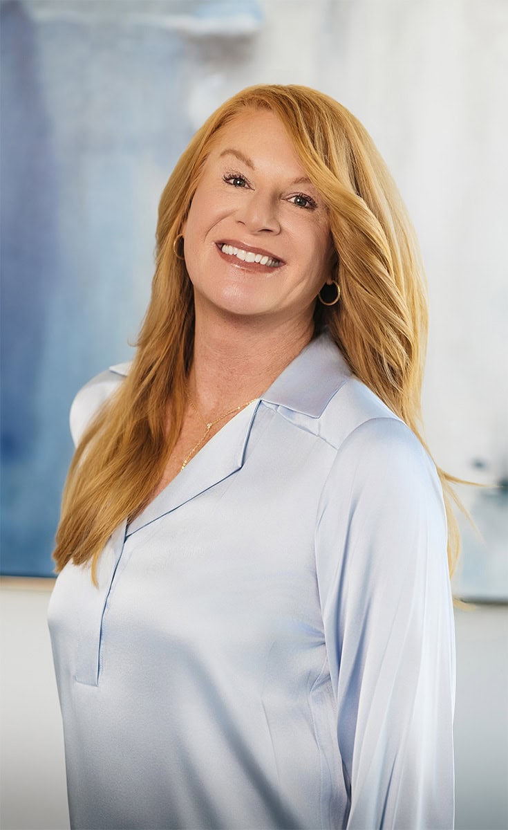 Smiling woman with long red hair in a white blouse at Arya Medical Spa.